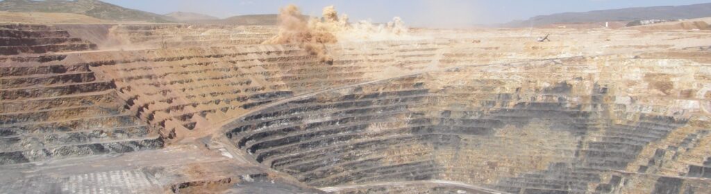 A photo of the Twin Creeks gold mine in Nevada, a visually striking strip mine. There's blast seen near the top of several layers cut into the earth